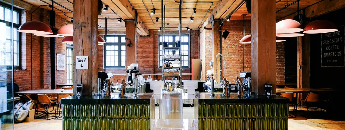 The Phil & Sebastian bar in the Simmons Building, with green tiled counter fronts, espresso machines, timber posts and red brick walls under a wooden ceiling