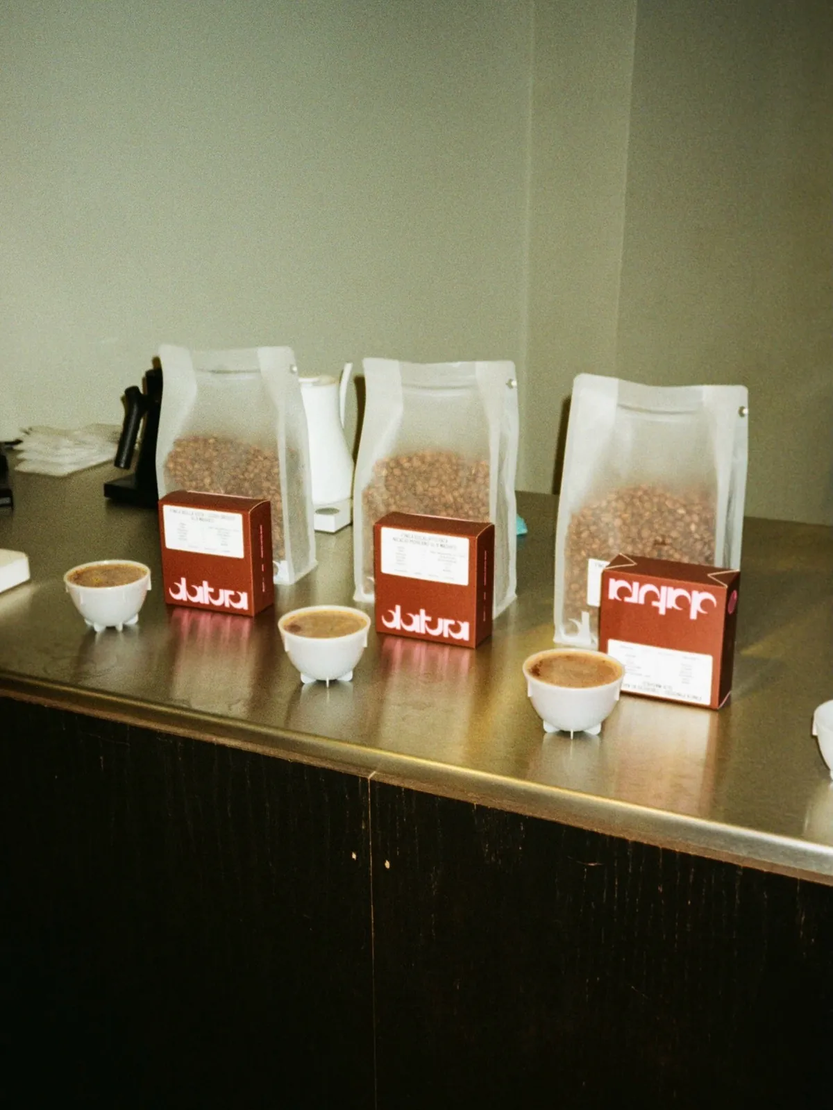 Cupping bowls in front of bags and boxes of guest coffees, among them Datura, lined up on a steel counter at 2323 in Sheffield
