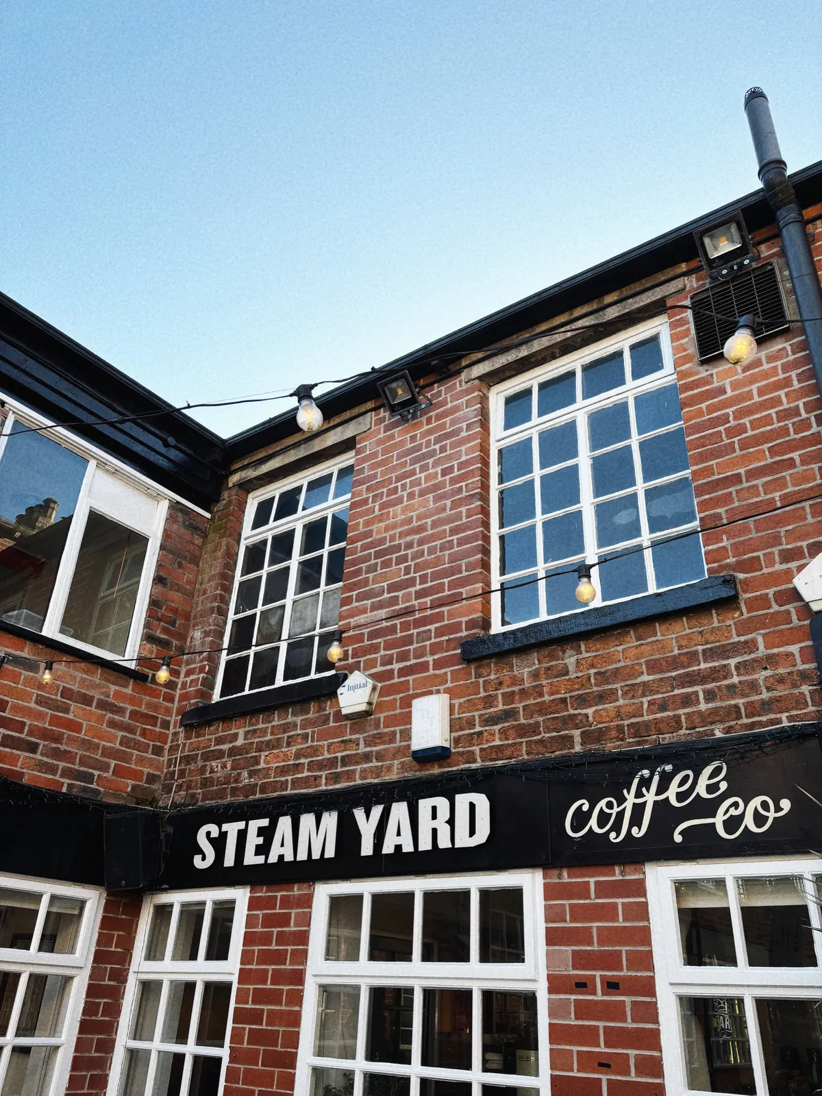 The black Steam Yard Coffee Co sign above the windows of the red-brick courtyard building in Sheffield's Devonshire Quarter