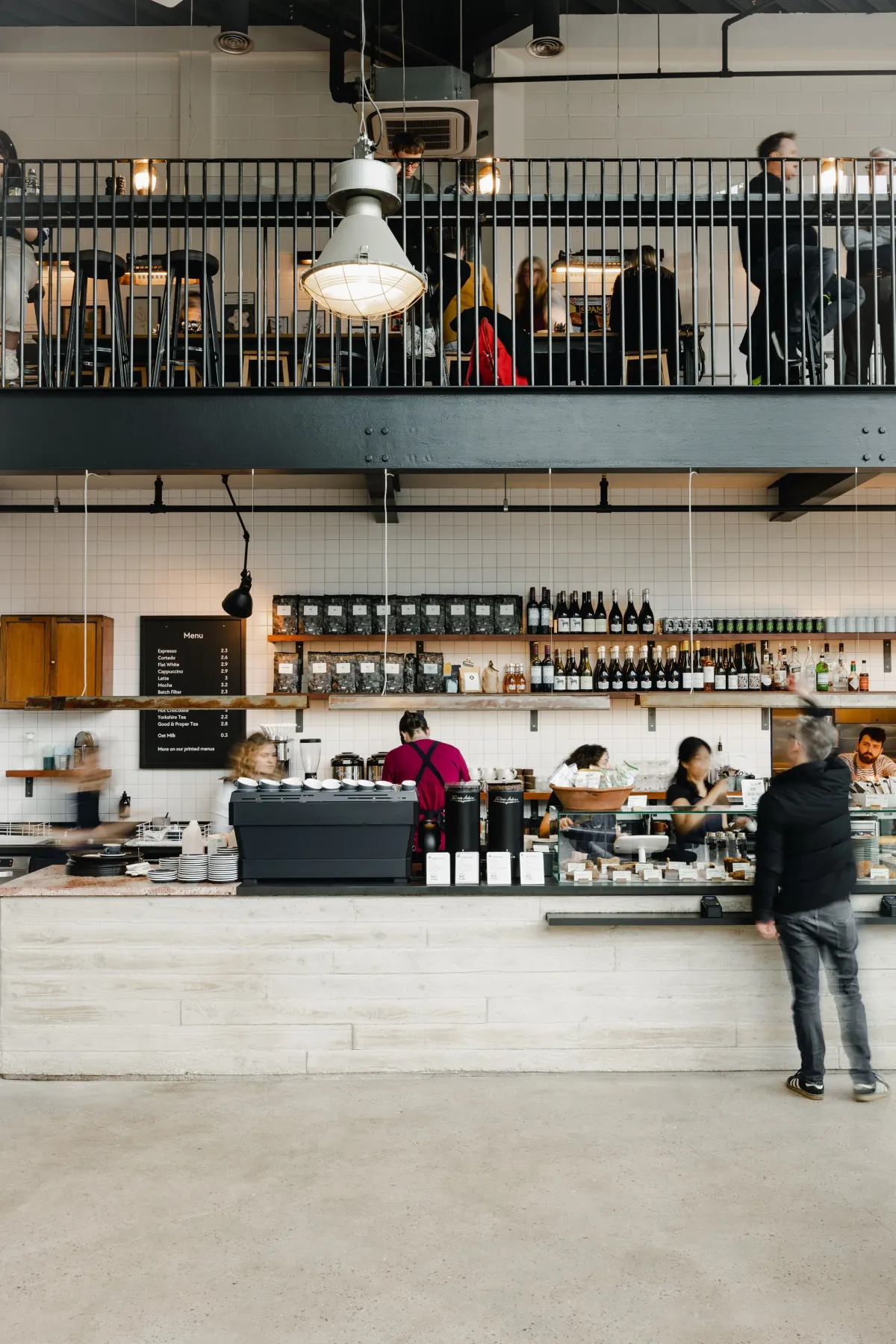 The long white counter at Marmadukes’ coffee flagship in Sheffield city centre, with a mezzanine above, shelves of bottles and a barista at the espresso machine