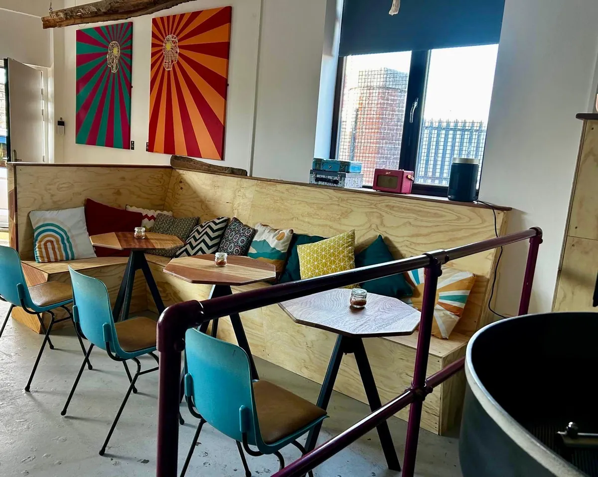 Plywood banquettes with cushions, teal chairs and round tables in the Smith Street coffee shop, with sunburst prints on the wall