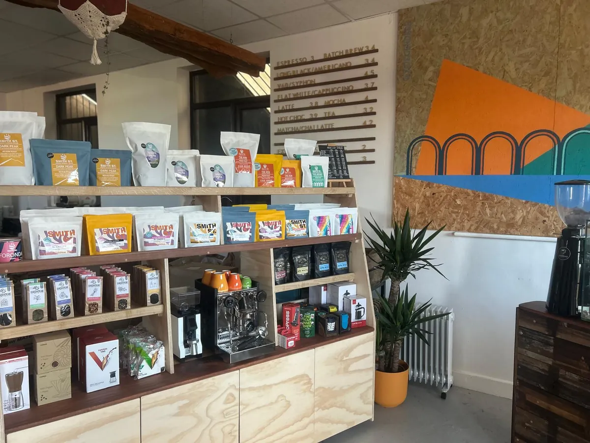 The retail shelves at Smith Street Coffee Roasters in Sheffield, stocked with bags of coffee, brewing gear and a grinder, with an orange and teal mural on the wall