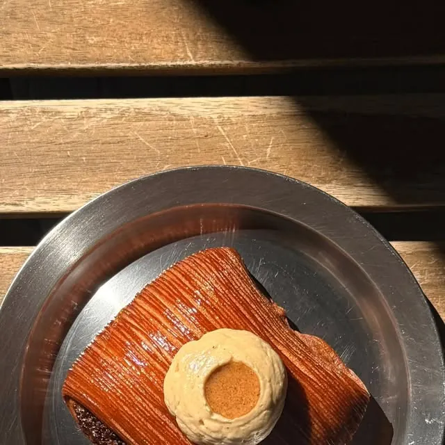 A pain suisse with hazelnut frangipane and a round of coffee cream on a metal plate, set on a sunlit wooden bench at Blackbird