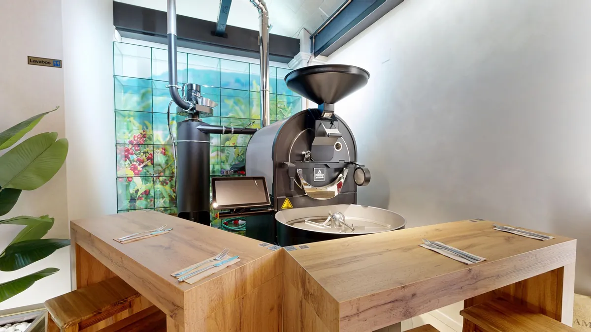 The Probat roaster at BOSCON in Valencia, behind wooden tables set with cutlery, in front of a green and blue tiled wall