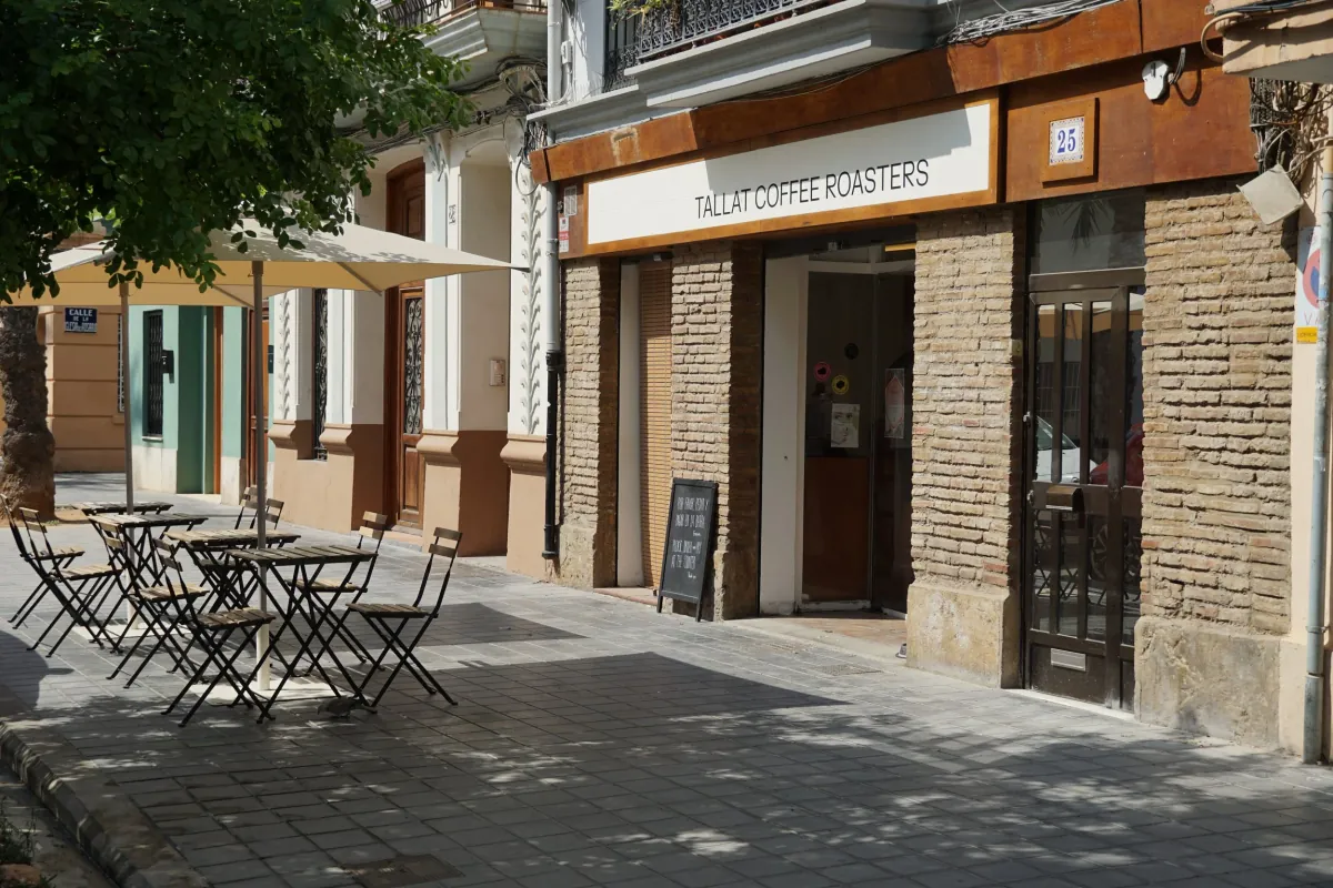 The brick front of TALLAT Coffee Roasters in El Cabanyal, with its white sign, a parasol and folding tables on the pavement