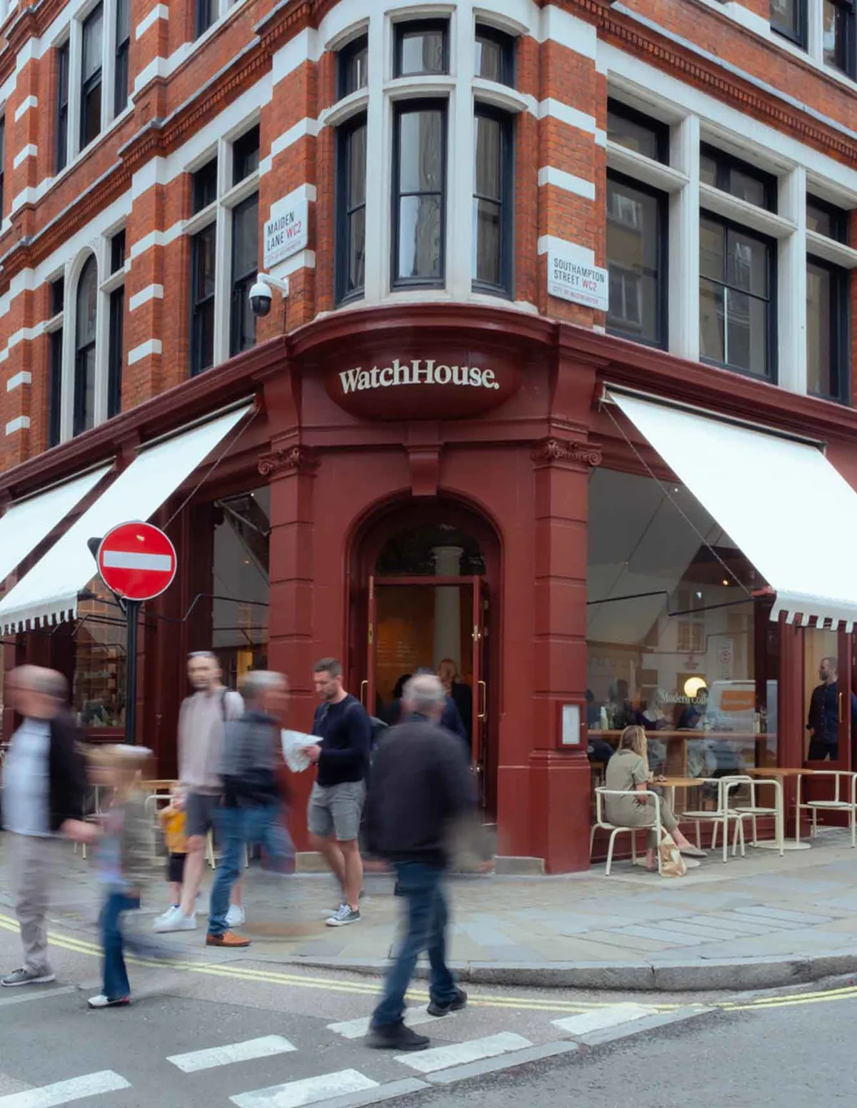 The red corner shopfront of WatchHouse Covent Garden, with white awnings and pavement tables