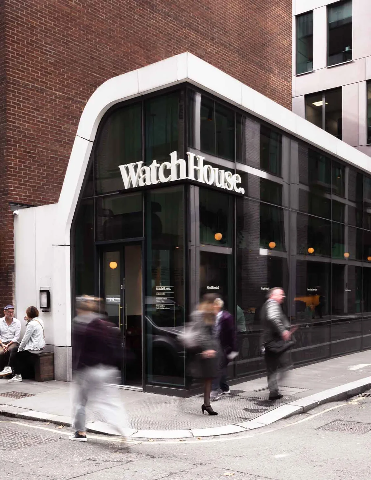 The curved glass corner front of WatchHouse Fetter Lane, framed in white, with people walking past