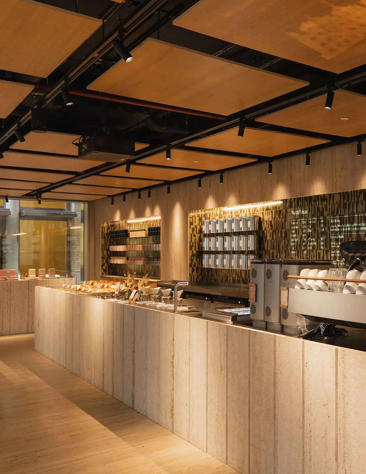 The long stone counter, espresso machine and retail shelves under timber ceiling panels at WatchHouse Hanover