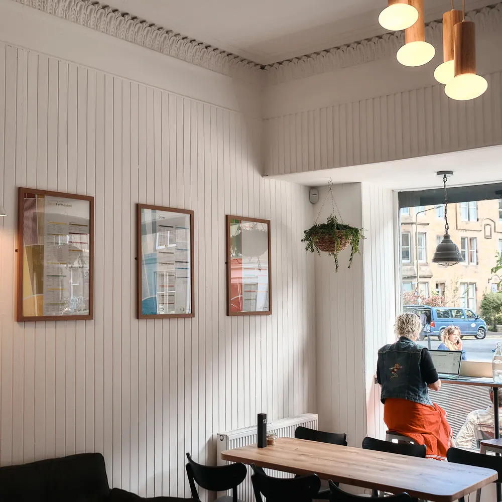 The white-panelled interior of Machina Marchmont, with framed menus on the wall and a customer at the window table