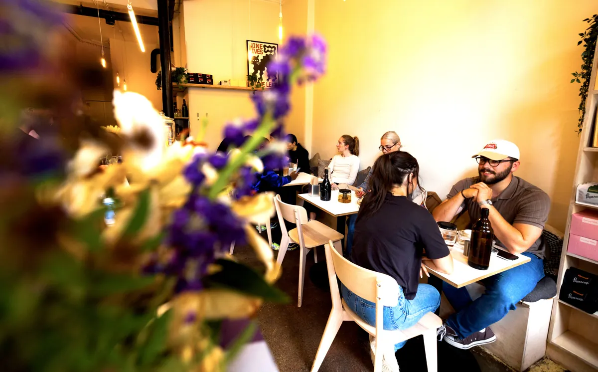 Customers at tables inside Papercup’s West End café, seen past a vase of flowers