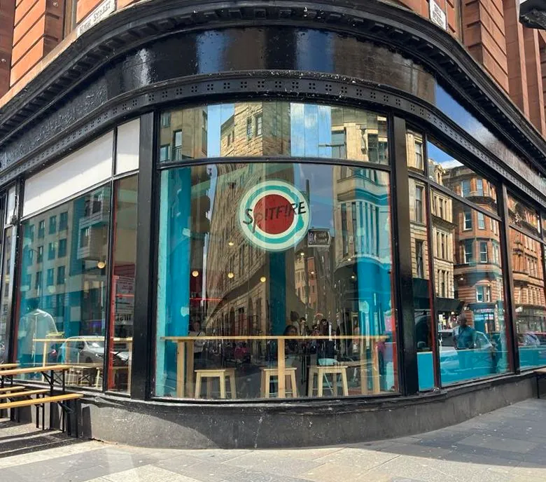 The glass-fronted corner café of Spitfire in the Merchant City, with its round logo in the window and bench seating outside