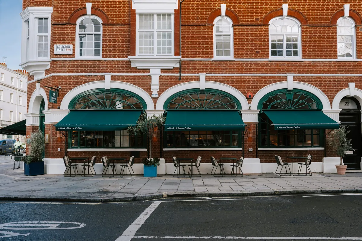 The red-brick corner of Workshop Cafe and Academy in Belgravia, with three green awnings, arched windows and pavement tables