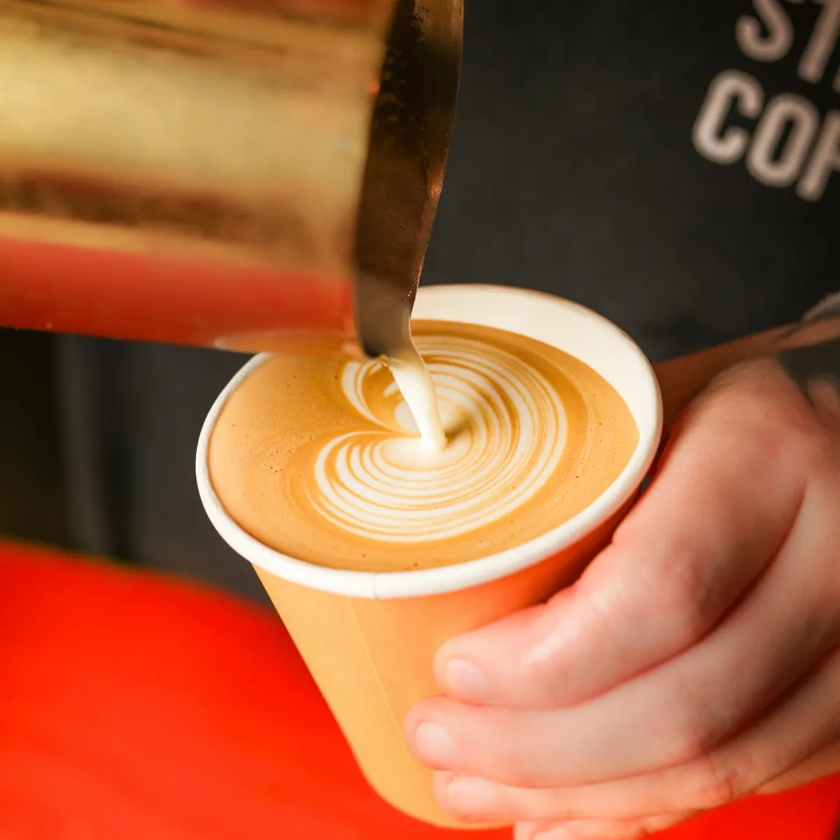 A barista pouring latte art into a takeaway cup at Bold Street Coffee