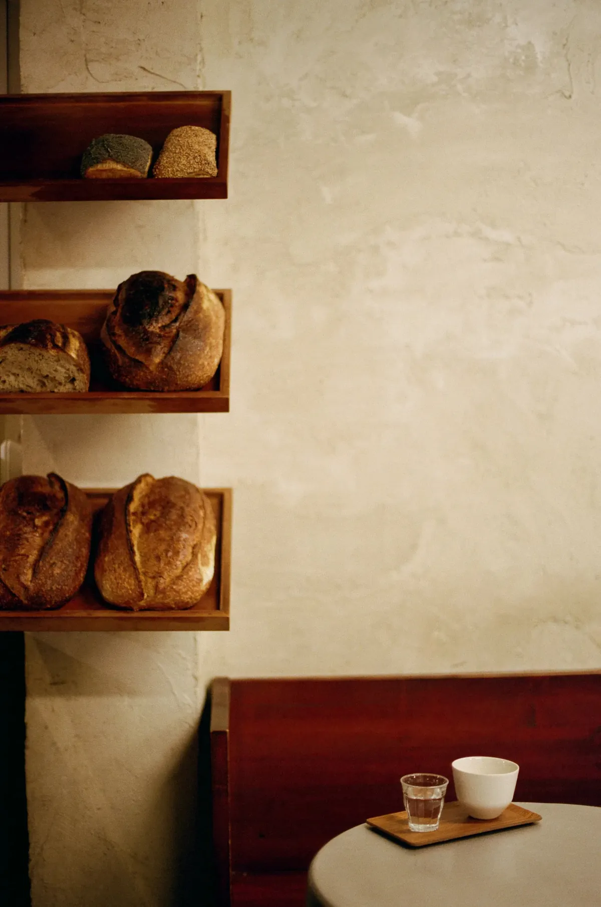 Loaves of sourdough on wooden shelves beside a bench and a cup at ACID Bakehouse