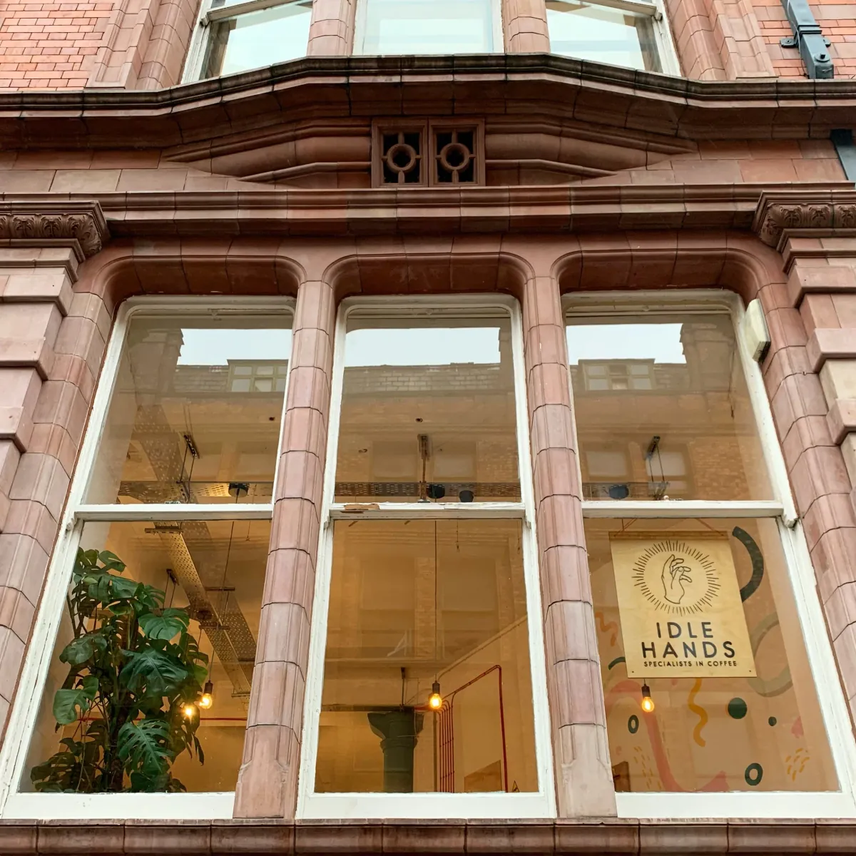 The red-brick façade of Dale House with the Idle Hands sign in the window and a plant behind the glass