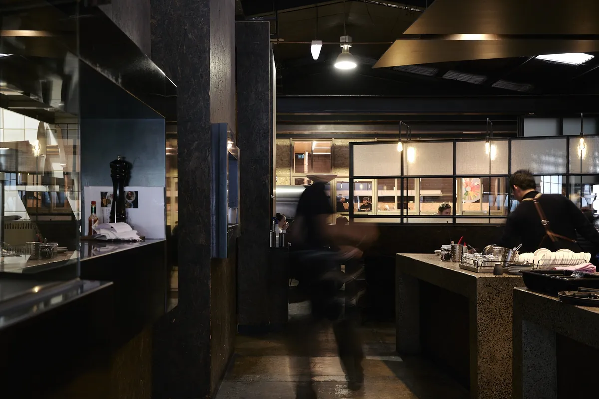 The dark interior of Code Black’s Brunswick café, with concrete tables, pendant lights and staff behind the pass
