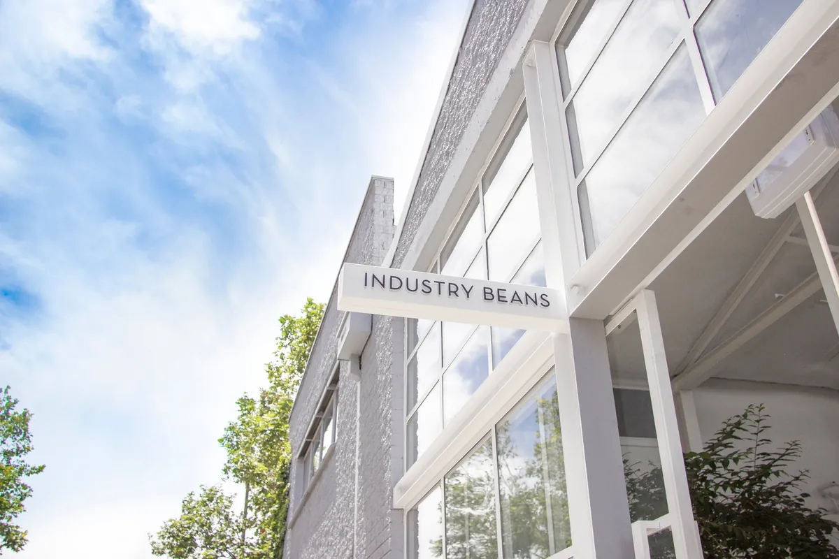 The white-painted warehouse of Industry Beans in Fitzroy, with the sign above the glass front and blue sky behind