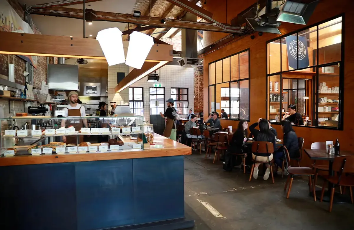 The warehouse interior of Seven Seeds Carlton, with a blue counter, pastry case and customers at wooden tables