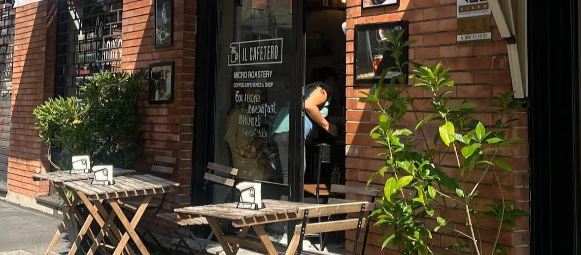 The brick façade of Il Cafetero, with its micro roastery sign on the glass door and wooden tables on the pavement