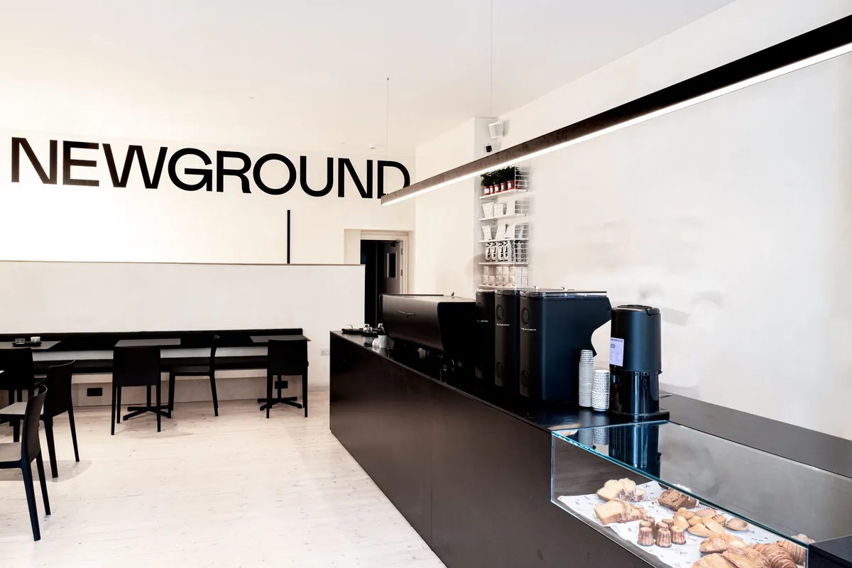The black counter and pastry case inside NewGround’s city-centre café in Oxford, with the NEWGROUND name across the white wall