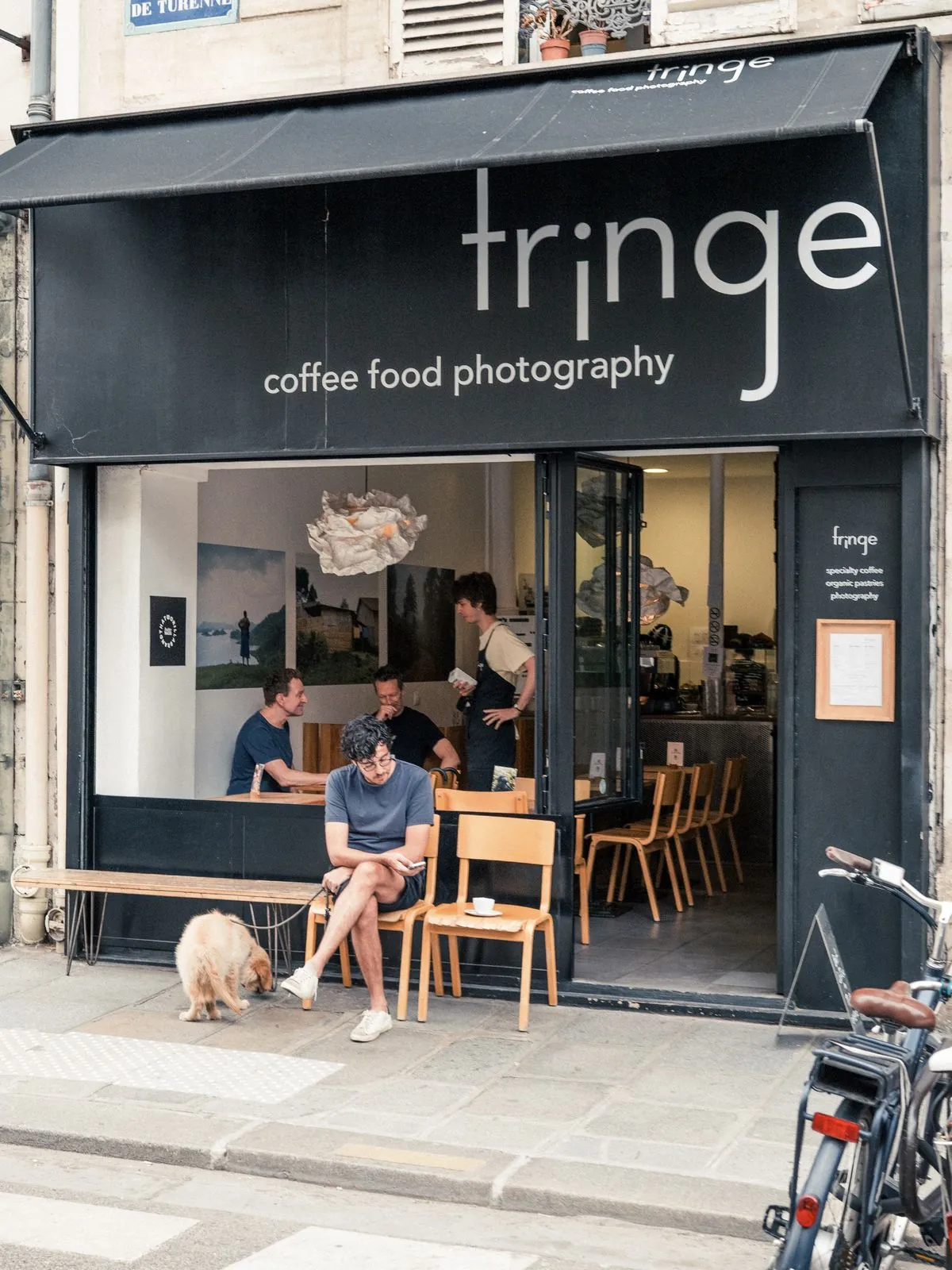 The black awning of Fringe, reading coffee, food, photography, with customers at the window and a bench outside