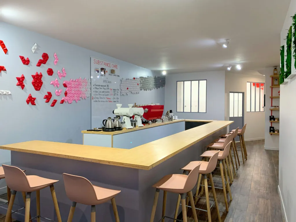 The pale wooden U-shaped bar at Substance Café, with pink stools, a red espresso machine and a board of special coffees on the wall