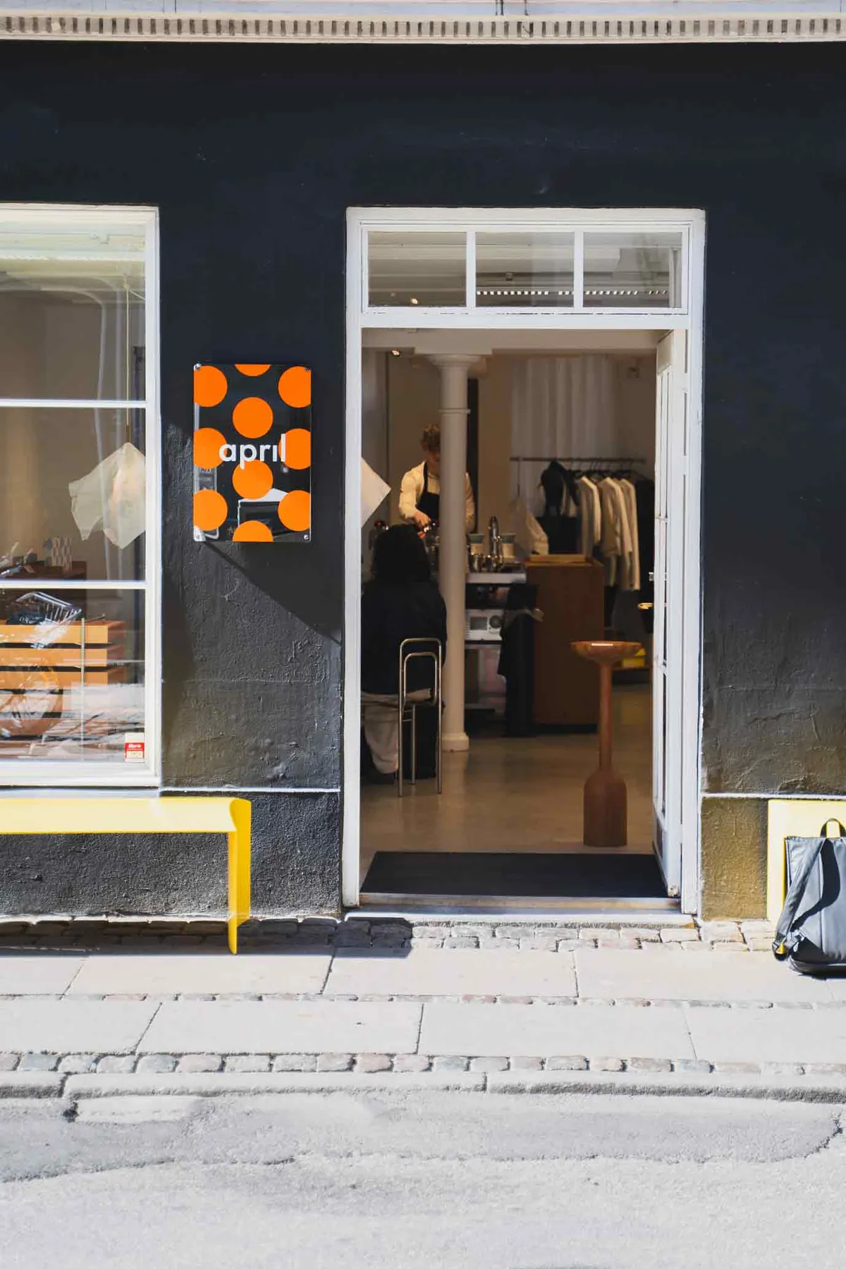 The doorway of the April Store, a narrow shopfront with a white door frame and an orange sign on a dark façade