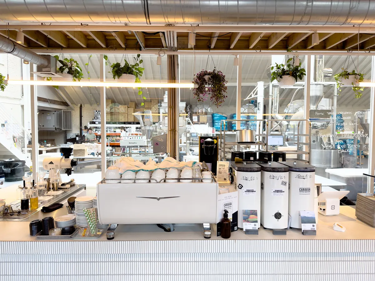 The Lambworks brewbar at Caravan, a long white counter with espresso machines and grinders in front of the glass-walled roastery