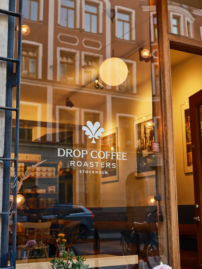 The Drop Coffee café window in Stockholm, with the Drop Coffee Roasters logo on the glass and lamps glowing inside