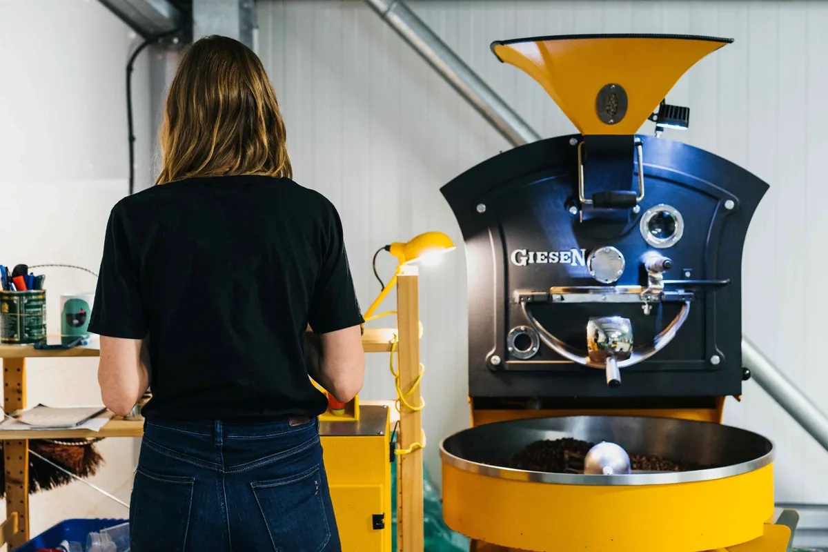 A roaster standing at the yellow Giesen roaster at Girls Who Grind Coffee