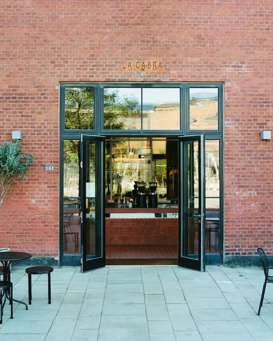 The entrance of La Cabra's Nordhavn roastery café, a tall glass door in a red brick wall