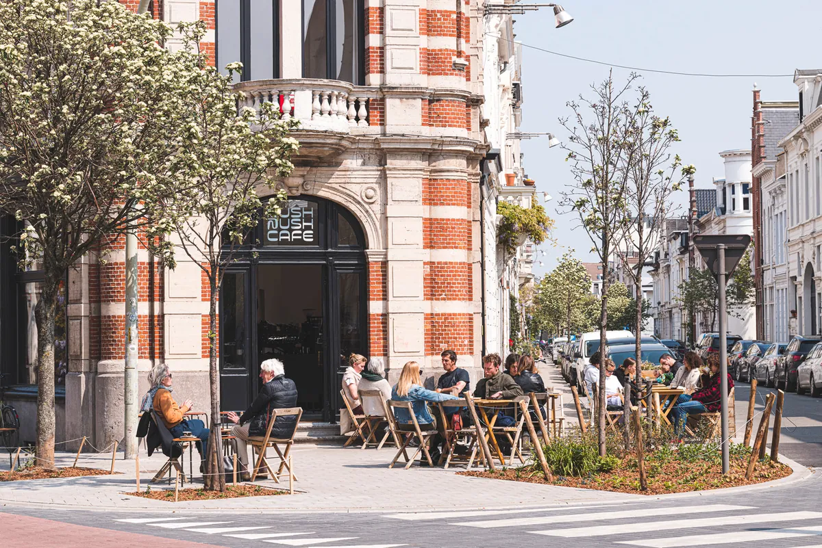 The Rush Rush café terrace on a corner in Zurenborg, with people at tables under trees beside tall townhouses