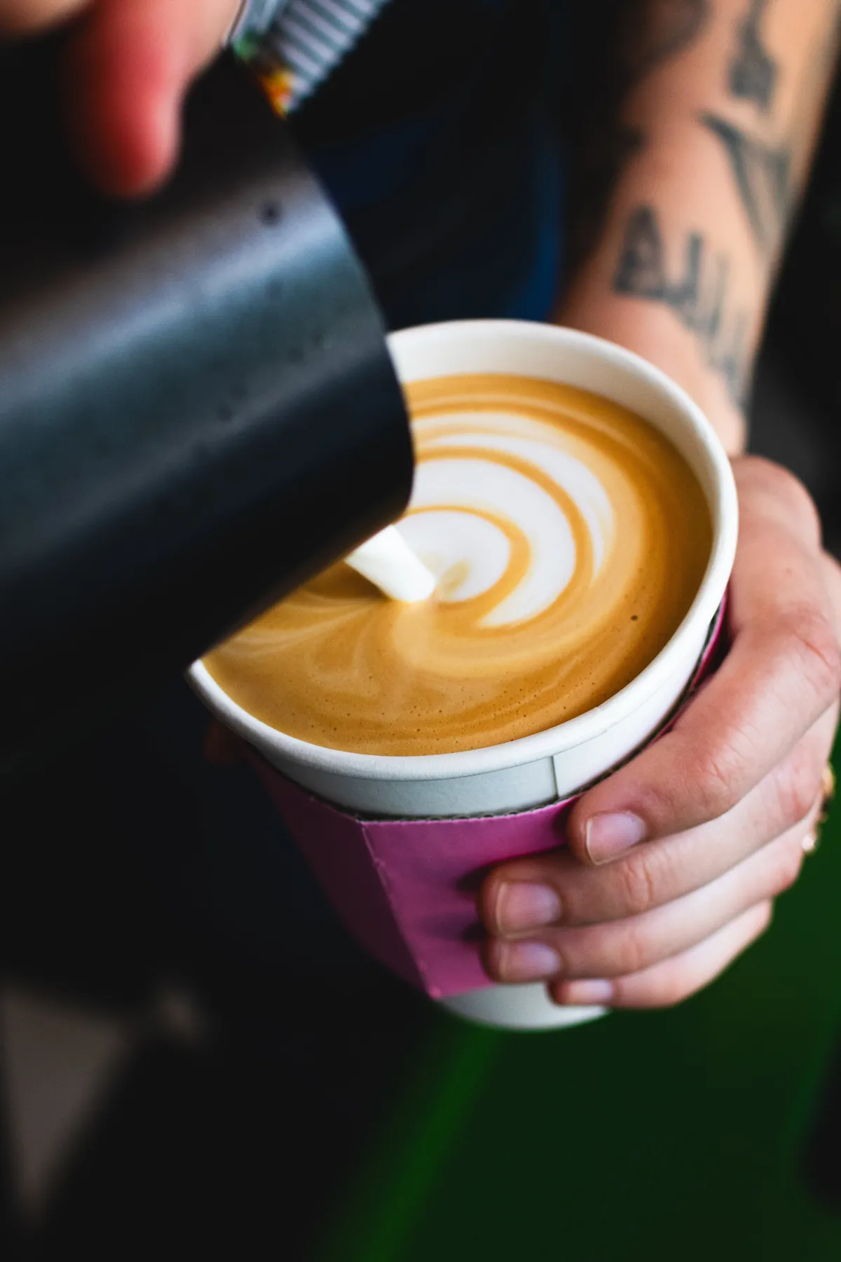 A barista pouring latte art into a paper cup at Sightseer's coffee bar
