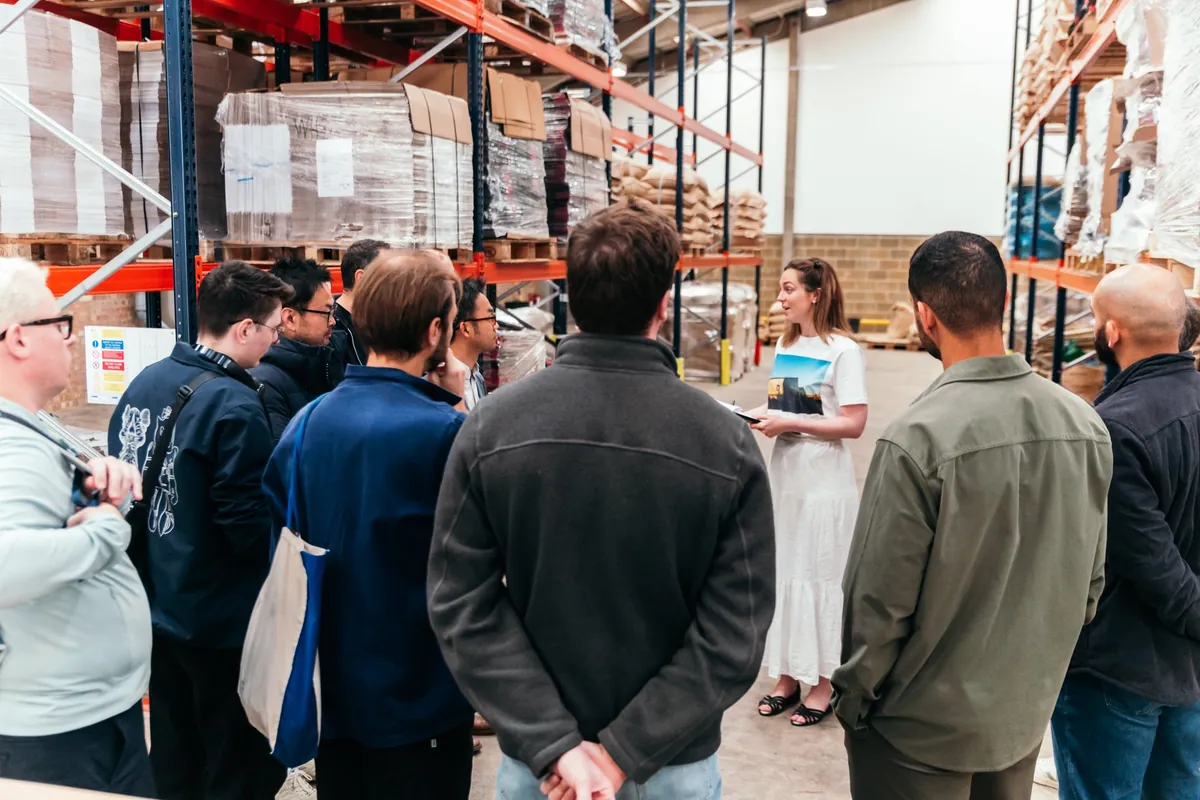 Visitors on a tour of the Square Mile roastery, gathered among racks of coffee