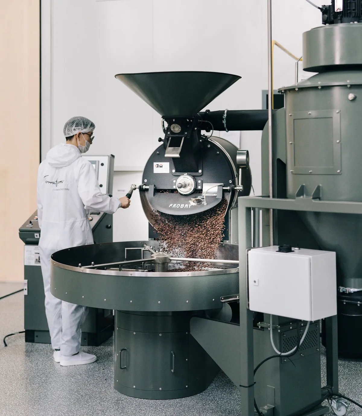 A roaster in protective clothing at the drum roaster in the Terraform roastery