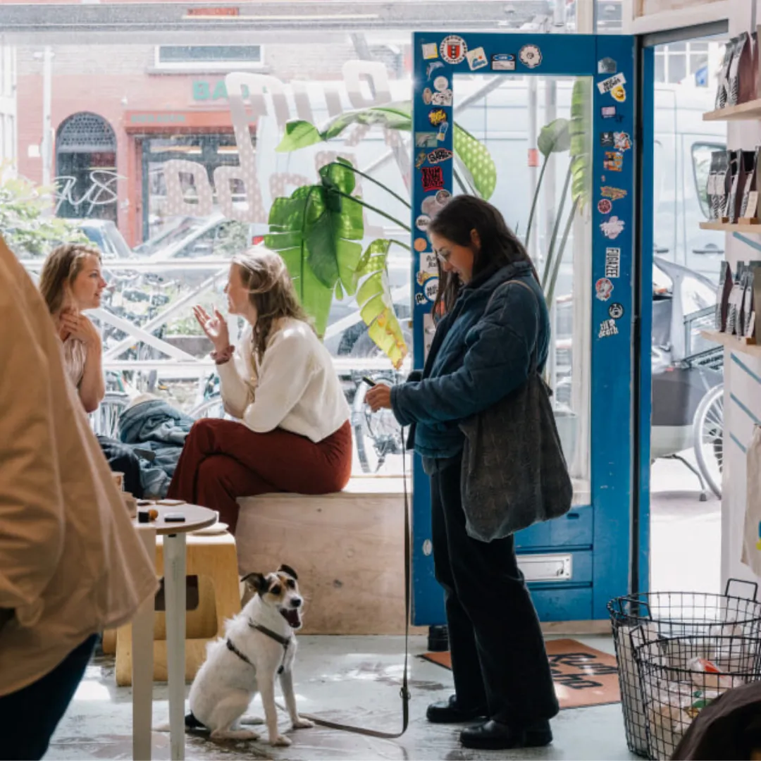 Customers and a dog inside a Rum Baba coffee shop, beside the open front door covered in stickers