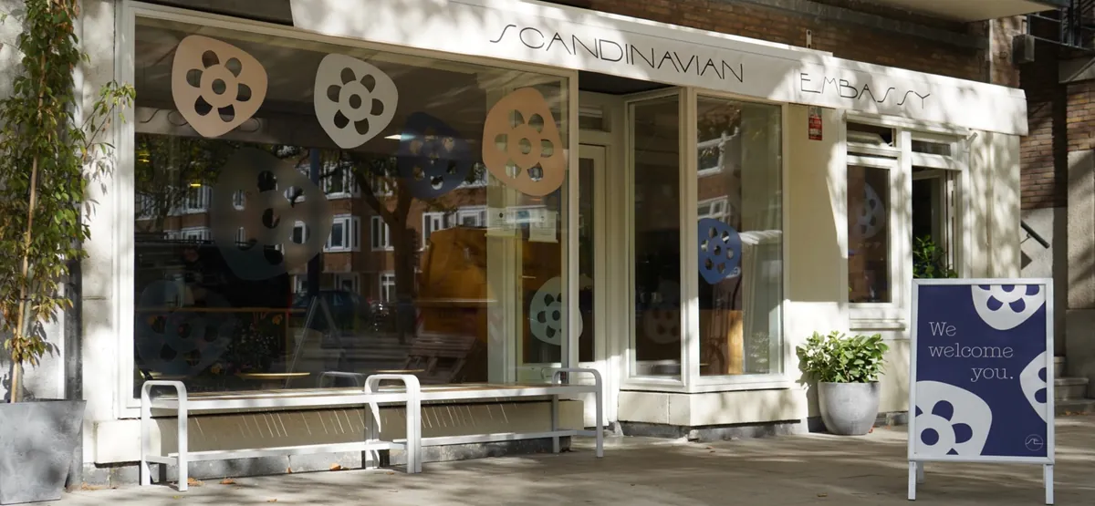 The shopfront of the Scandinavian Embassy café by the Sarphatipark, with a bench under the windows and a welcome sign on the pavement