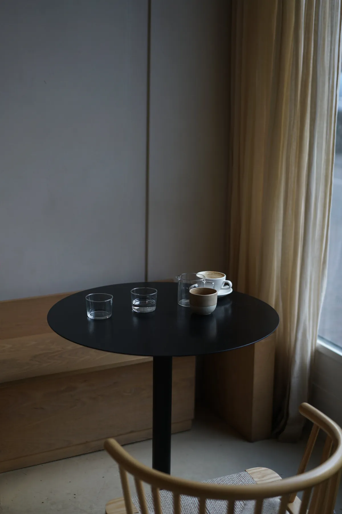 A round black table with coffee and glasses of water beside a curtained window in the Uncommon café
