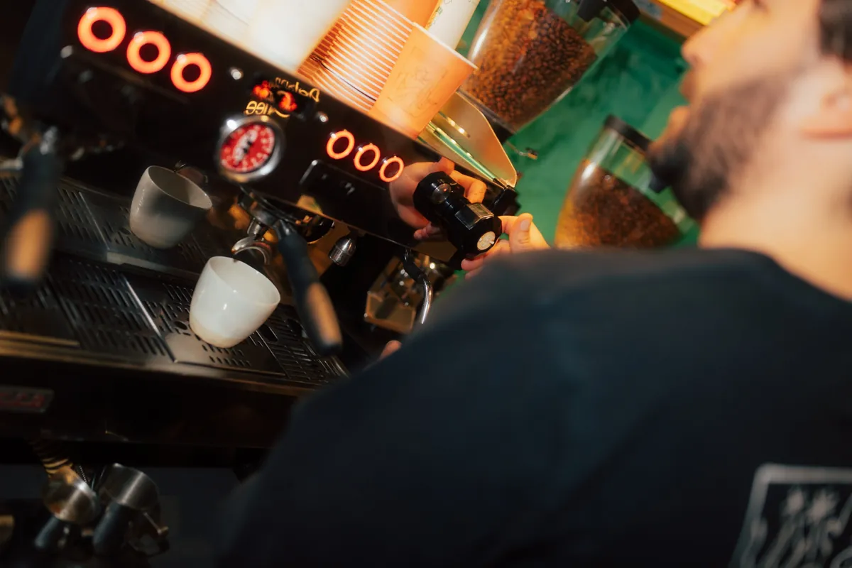 A barista pulling shots on the espresso machine at the Dalston Coffee bar in the Raval, with grinders lit behind