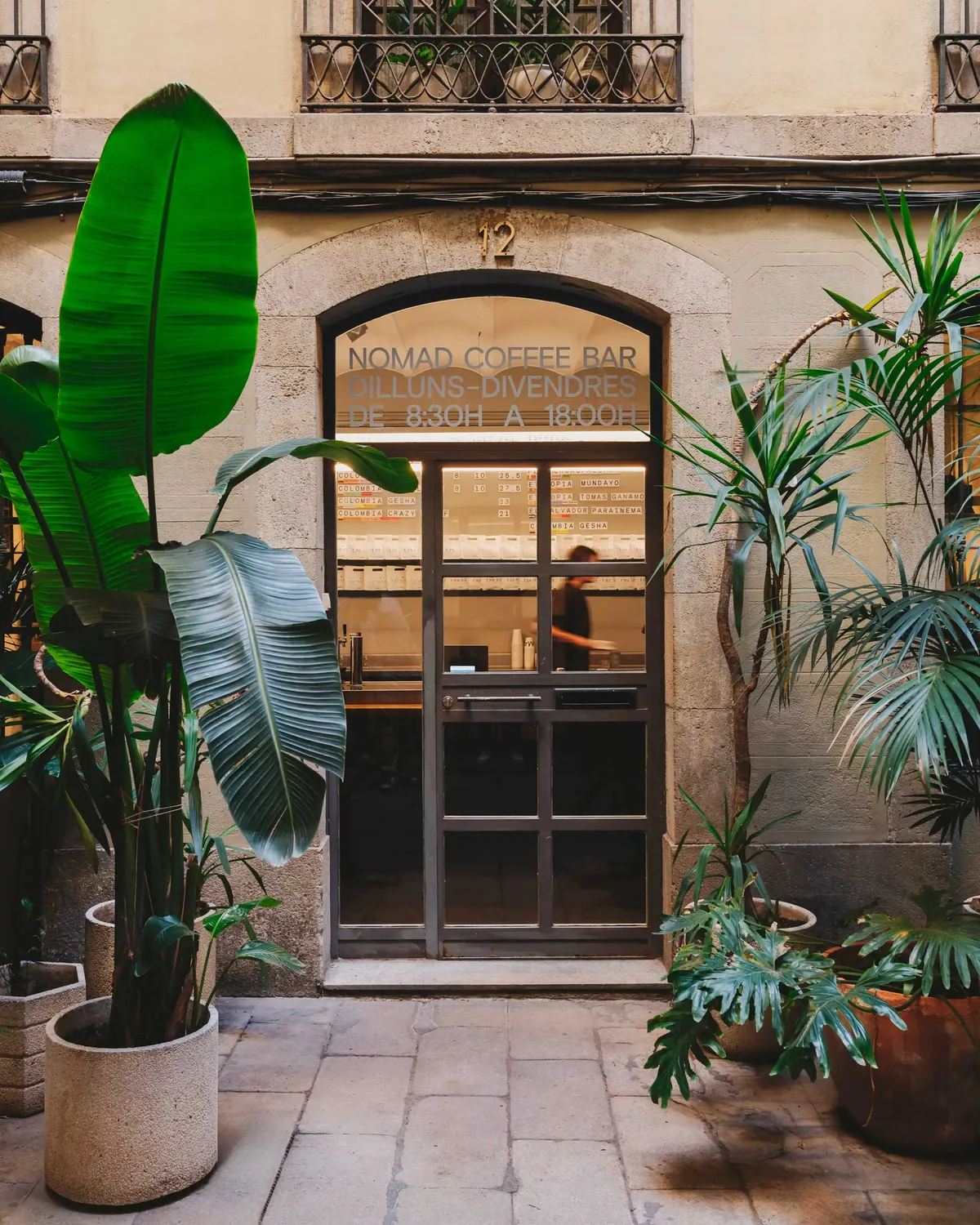 The arched doorway of the NOMAD Coffee Bar, framed by large potted plants in a paved passage