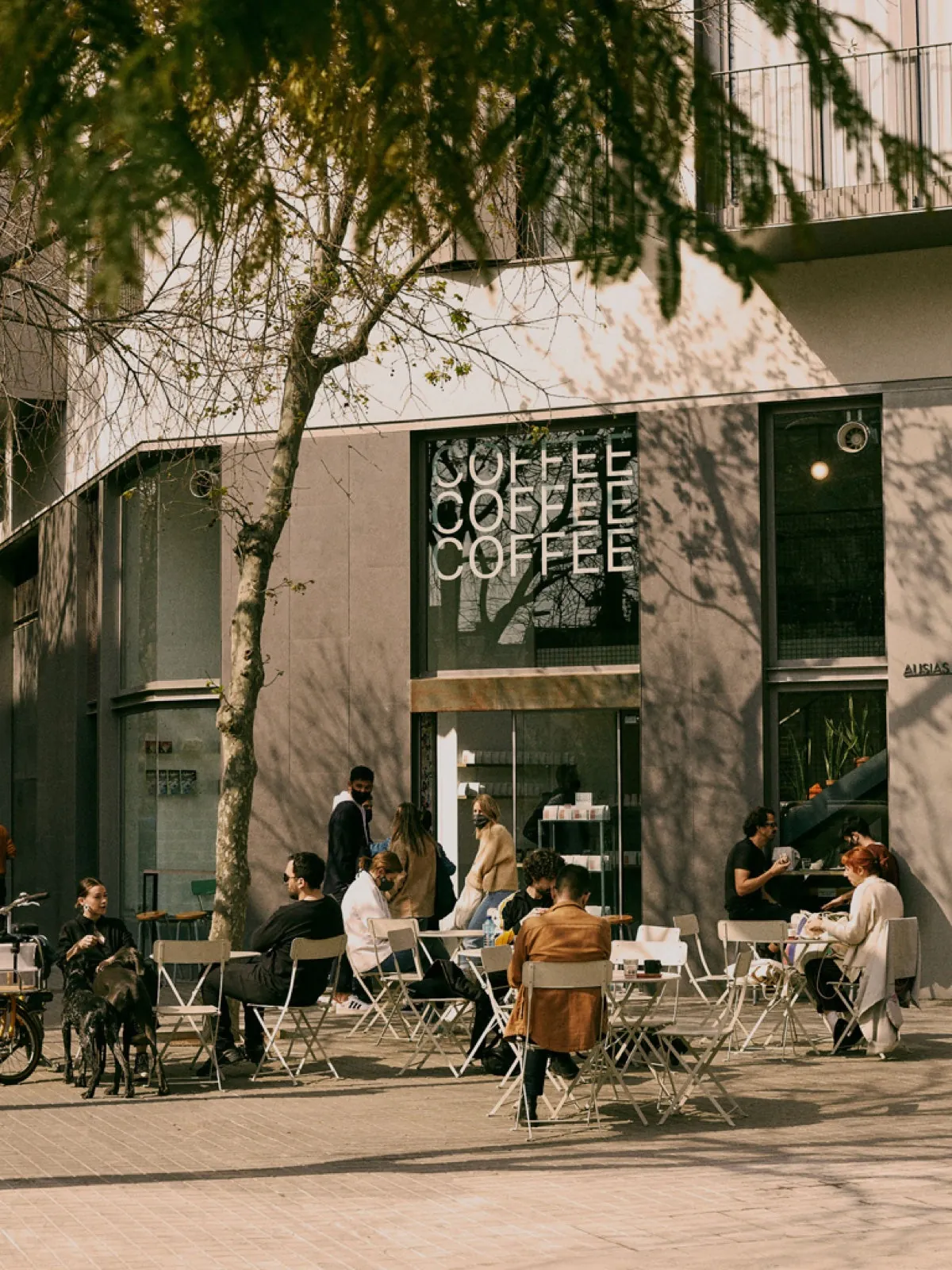 The Three Marks Coffee café in the Eixample, with people at terrace tables under a tree outside the shopfront