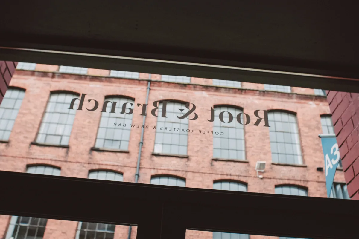 The Root & Branch Coffee Roasters & Brew Bar name lettered on the window, looking out at the red-brick Portview Trade Centre in Belfast