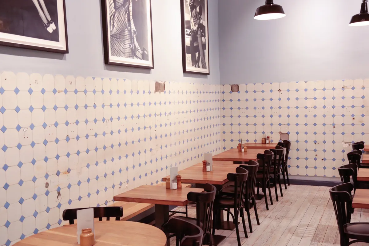 The dining room at Father Carpenter, with wooden tables, bentwood chairs and blue-and-white tiled walls under framed prints