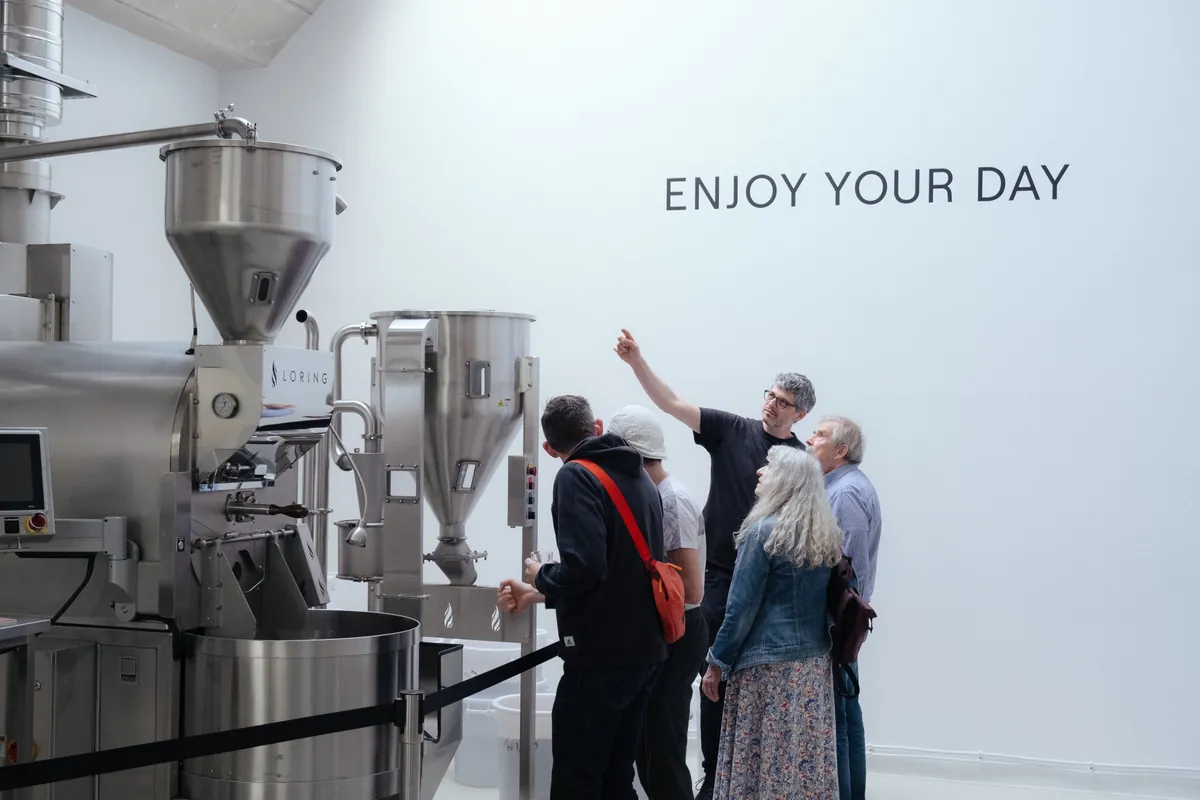Visitors gathered beside the roaster inside the white-walled NANO KAFFEE roastery