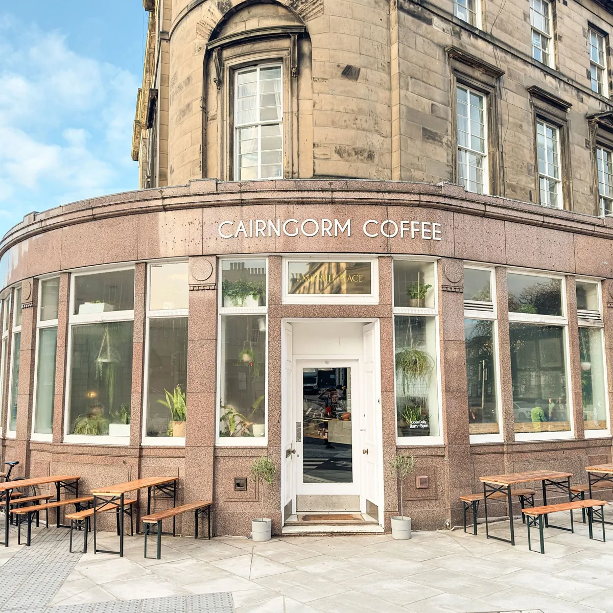 The curved granite corner shopfront of Cairngorm Coffee in the West End, with benches and tables set out on the pavement
