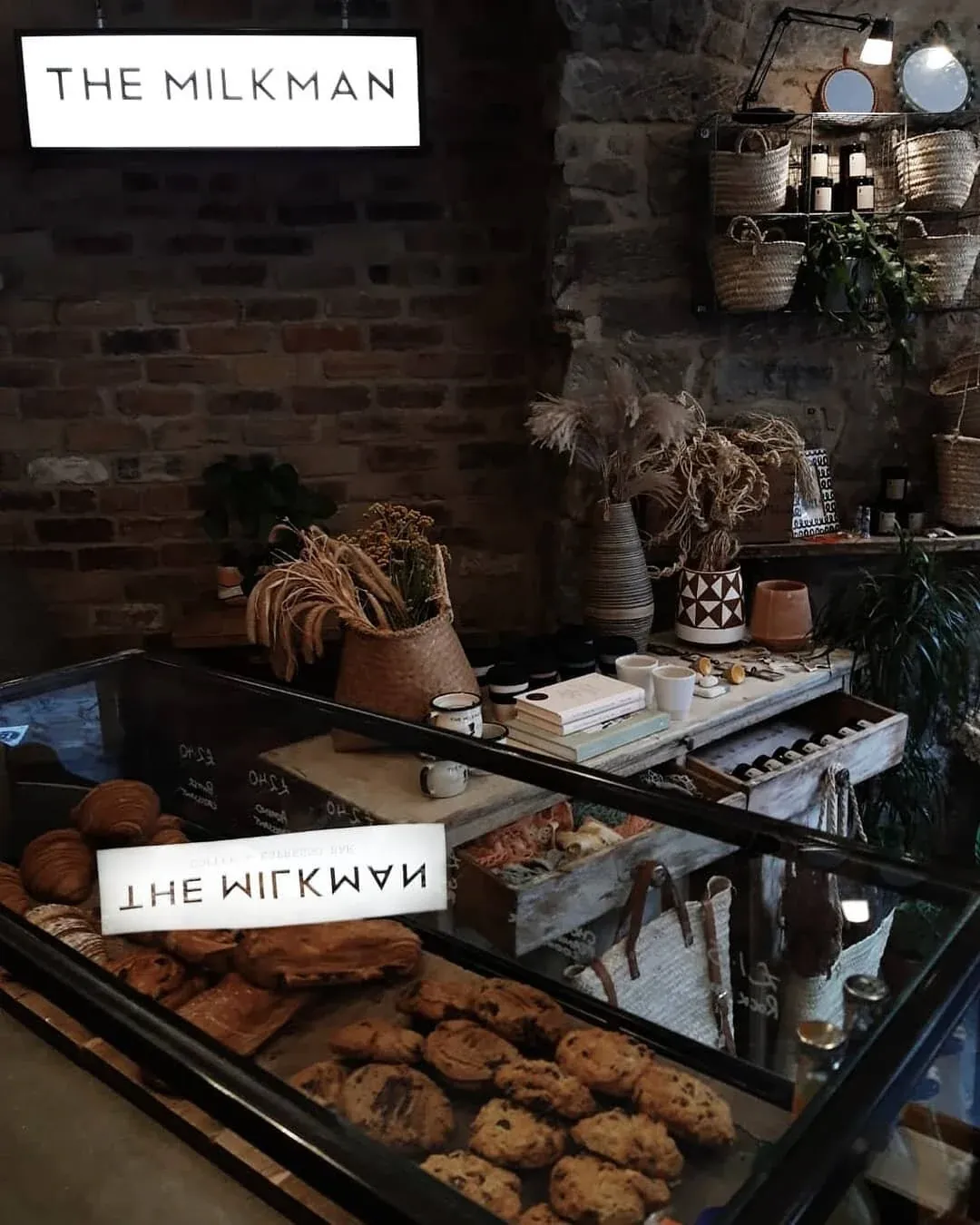 The pastry counter at The Milkman, with the café's sign above shelves of plants and dried flowers against a stone wall