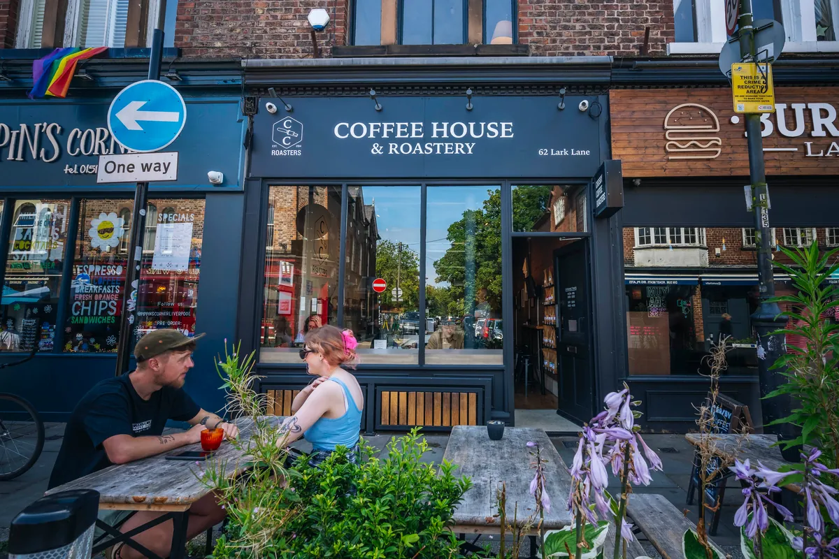 The navy shopfront of Crosby Coffee's coffee house in Aigburth, with people at wooden tables outside among flowering plants