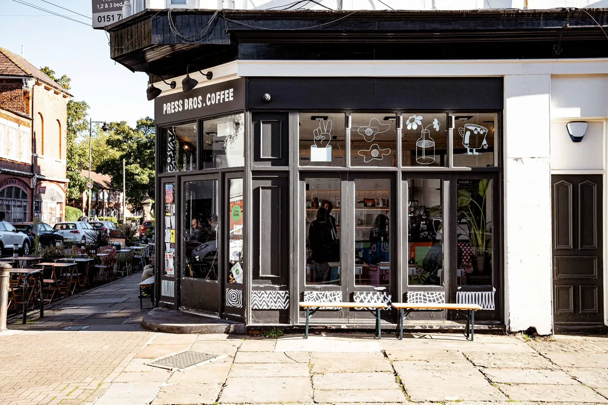 The black corner shopfront of Press Bros Coffee in Aigburth, with two benches beneath its tall windows