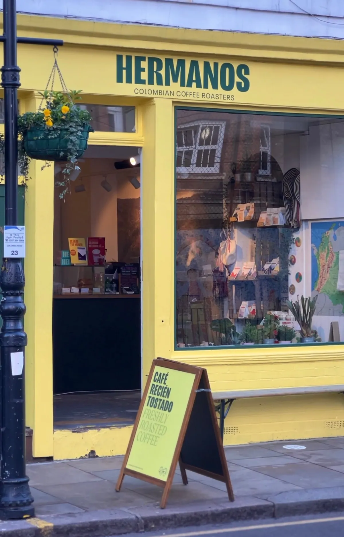 The yellow shopfront of Hermanos by the Columbia Road flower market, with a hanging basket and a pavement sign by the door