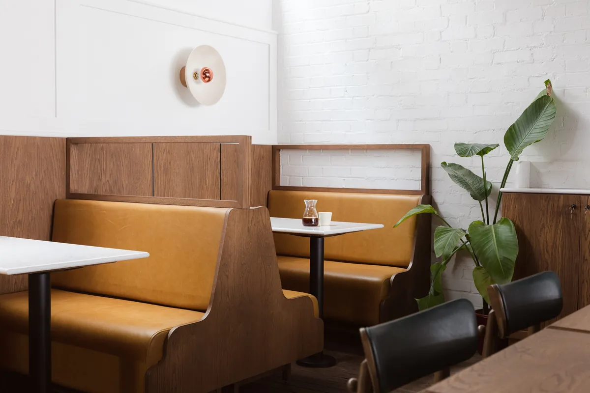 Leather booth seating and tables against a white brick wall inside Prufrock Coffee in Clerkenwell